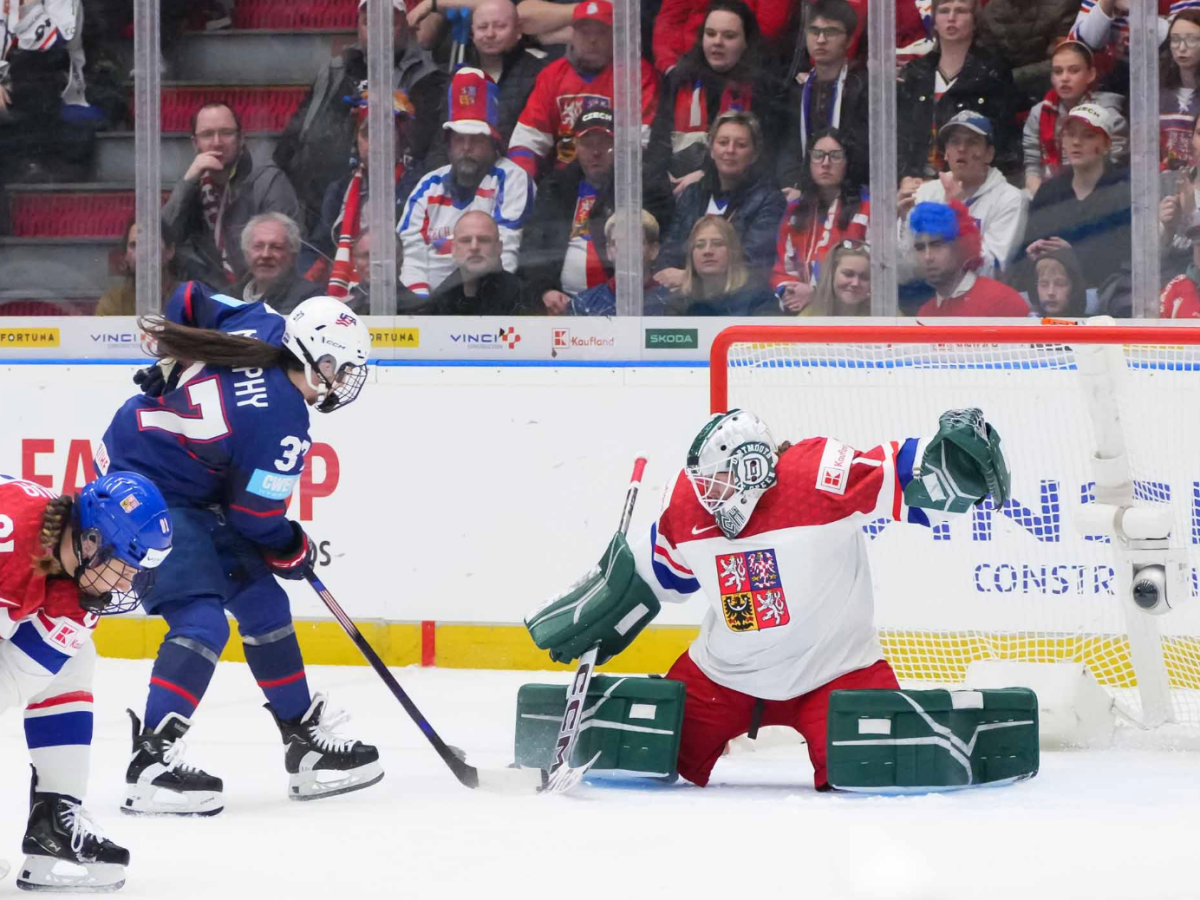 Murphy (in blue) prepares to shoot from right outside the crease, as Hesová (in white) slides to make a save.