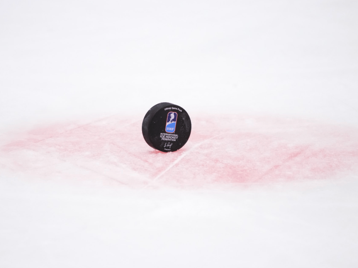 A puck with the IIHF logo stands on edge in one of the faceoff dots.