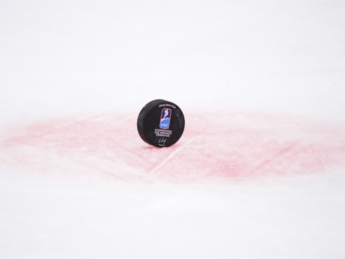 A black puck with the IIHF logo stands on edge in one of the  faceoff dots.