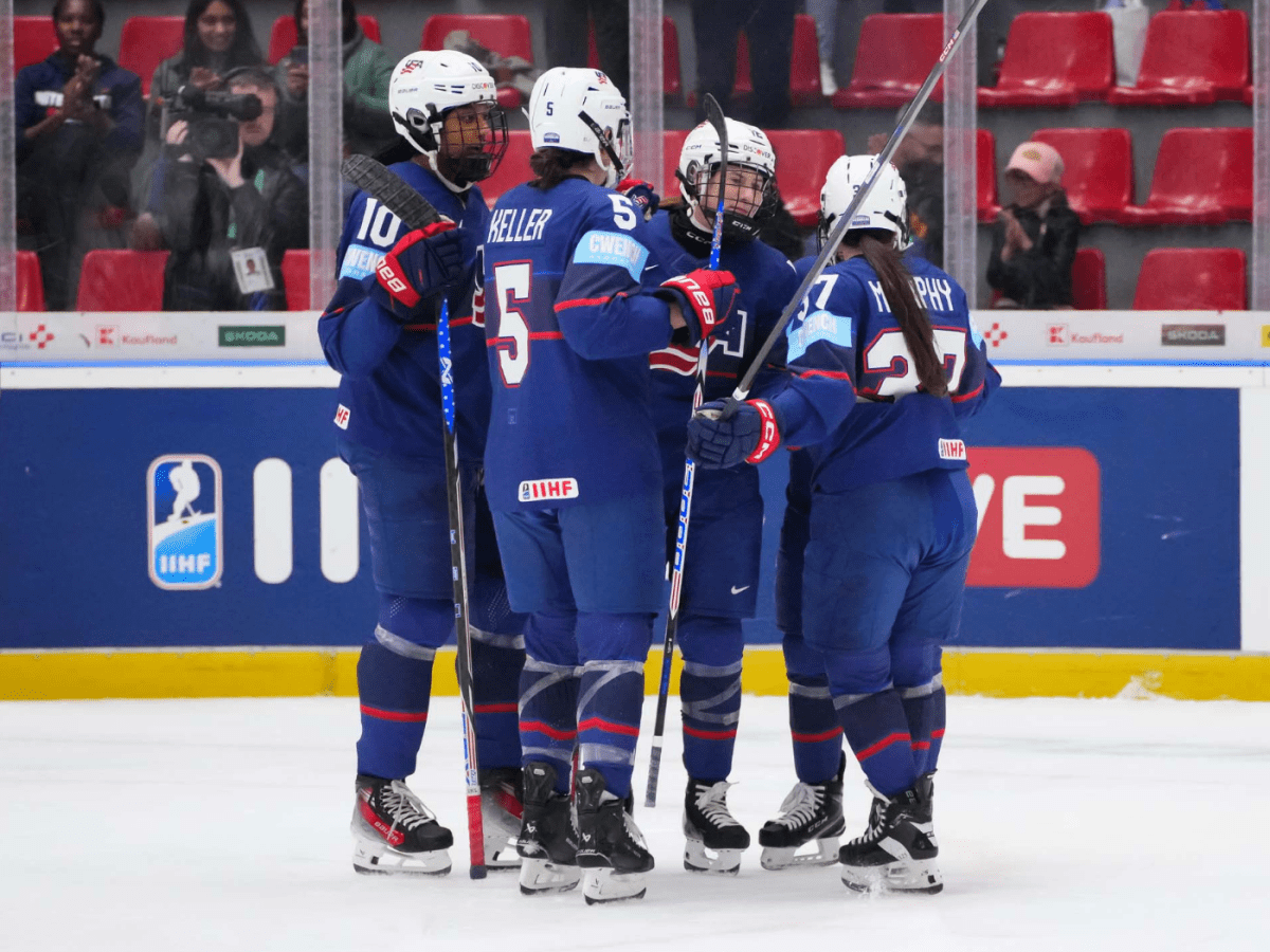 Four USA players celebrate with a group hug. They are wearing blue uniforms.