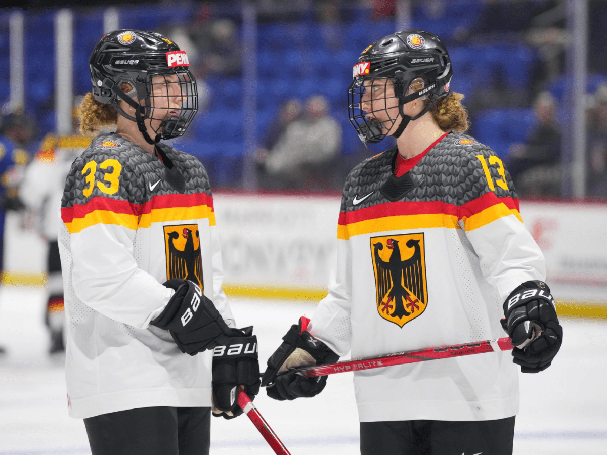 Lilli (left) and Luisa (right) stand near the blue line having a discussion. They are wearing away Germany uniforms.