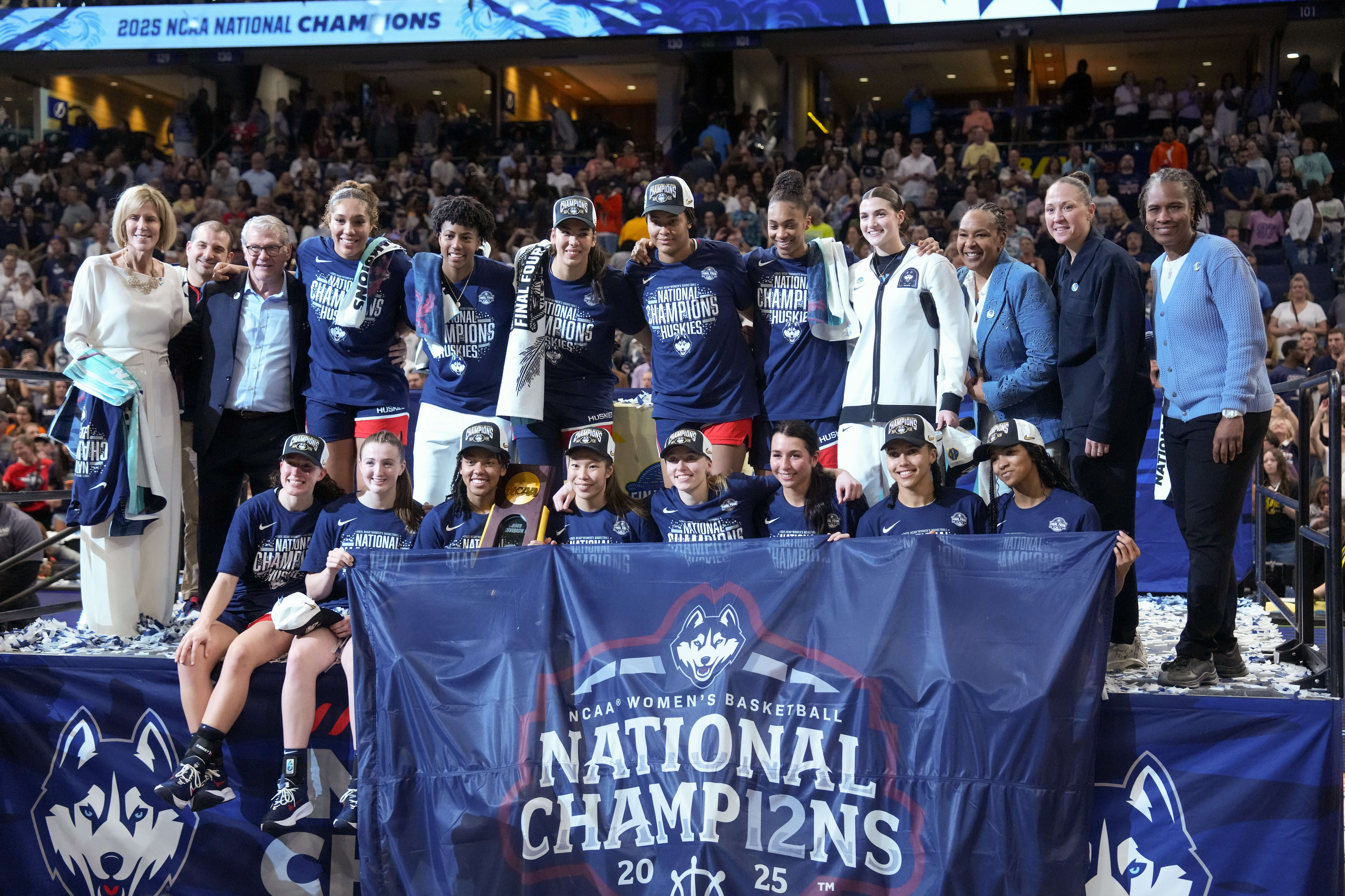UConn women's basketball poses with a large blue banner after winning the 2025 national championship.