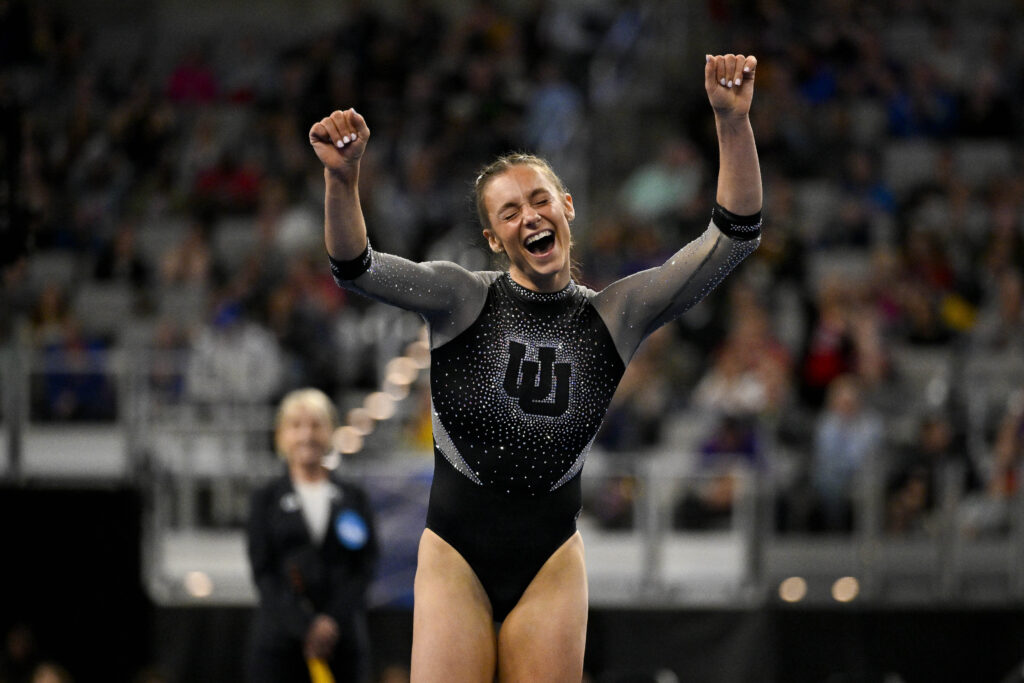 A gymnast in a black leotard with sparkles celebrates a successful routine.