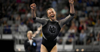 A gymnast in a black leotard with sparkles celebrates a successful routine.