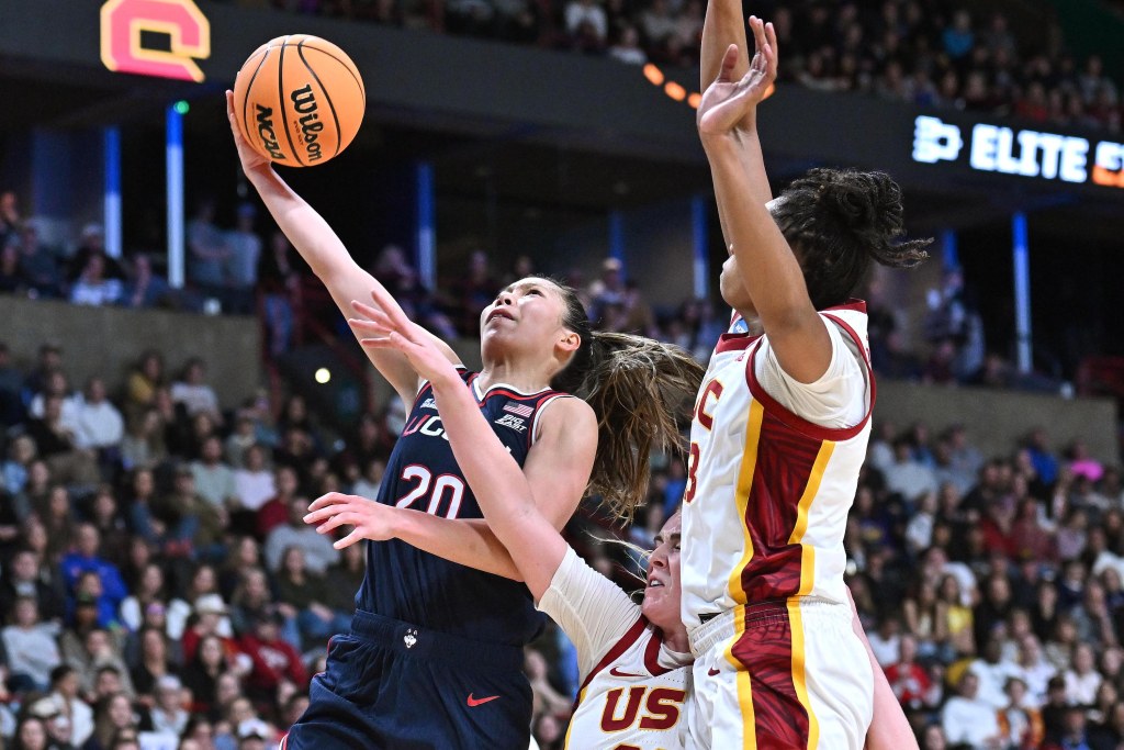 UConn guard Kaitlyn Chen extends her arm to shoot a right-handed layup around two USC defenders.