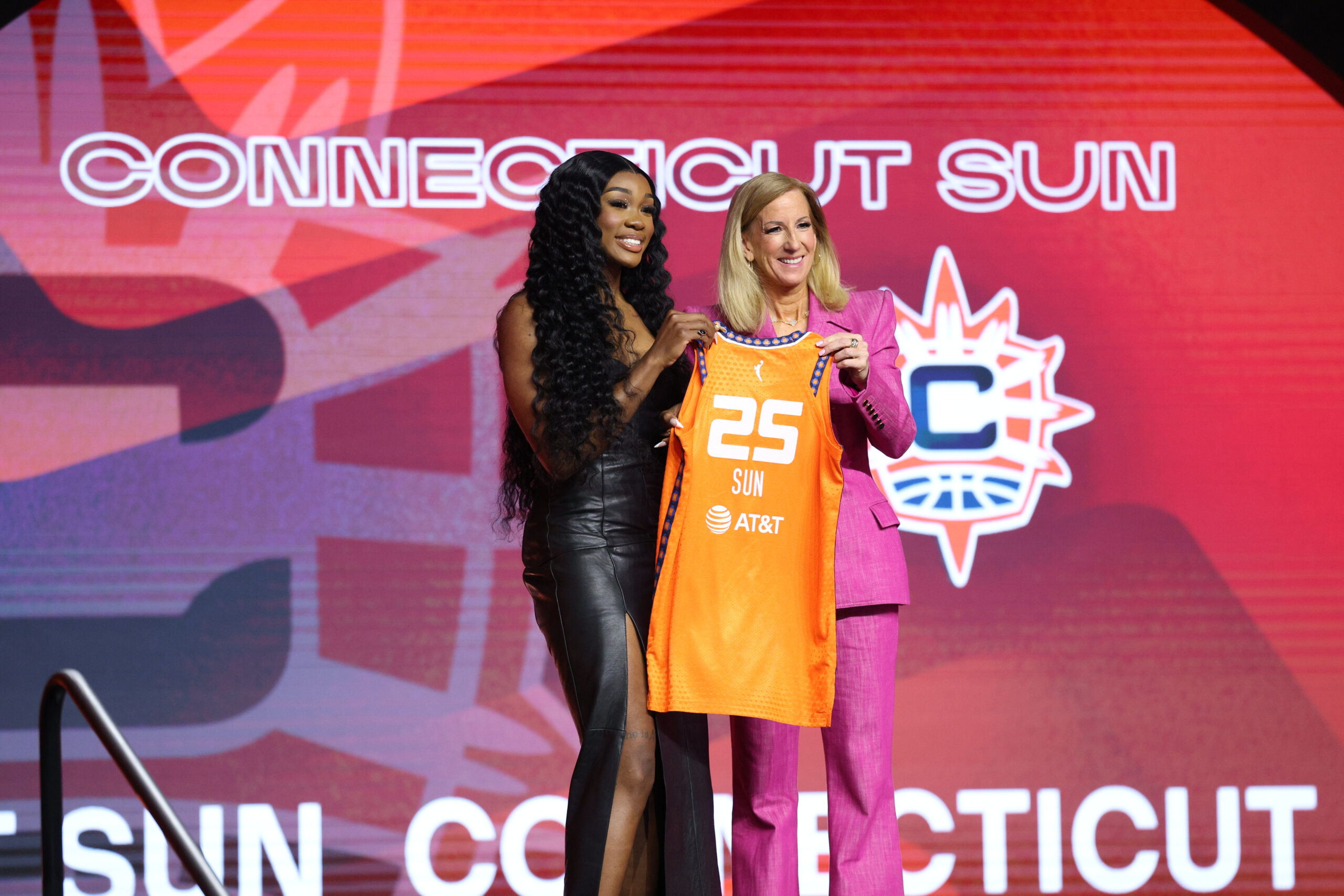 Aneesah Morrow holds jersey up with WNBA commissioner standing on the draft stage.