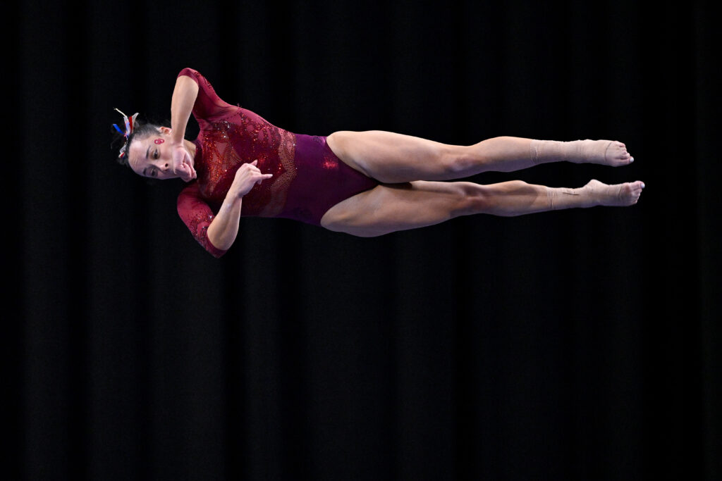 Wearing a red leotard, Oklahoma gymnast Faith Torrez twists in the air during a performance on balance beam.