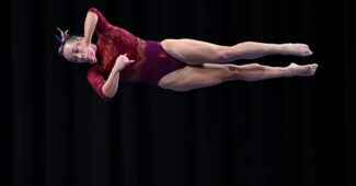 Wearing a red leotard, Oklahoma gymnast Faith Torrez twists in the air during a performance on balance beam.