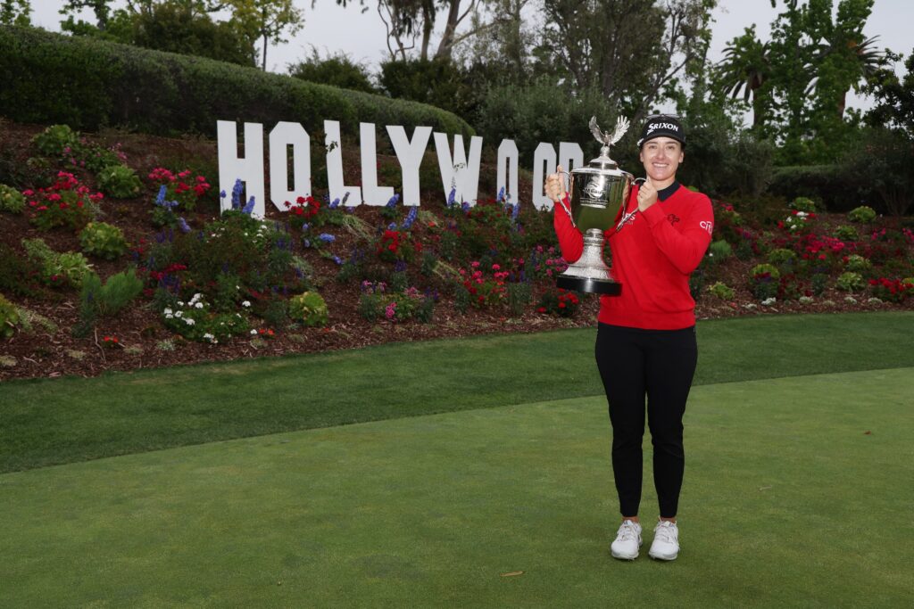 Hannah Green stands to the right in front of a miniature Hollywood sign at Wiltshire Country Club. She holds up the JM Eagle LA Championship trophy.