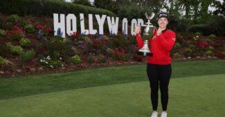 Hannah Green stands to the right in front of a miniature Hollywood sign at Wiltshire Country Club. She holds up the JM Eagle LA Championship trophy.