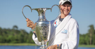 Nelly Korda, 2024 Chevron Championship winner, holds up the tournament trophy to her right and smiles.