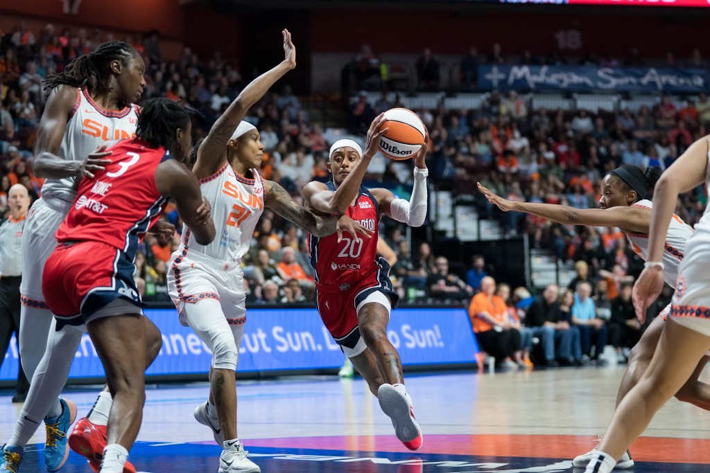 Washington Mystics guard Brittney Sykes holds the ball with both hands as she attacks the paint. One Connecticut Sun defender tries to stay on her hip, and another reaches from the opposite side but can't get close enough to slow Sykes.