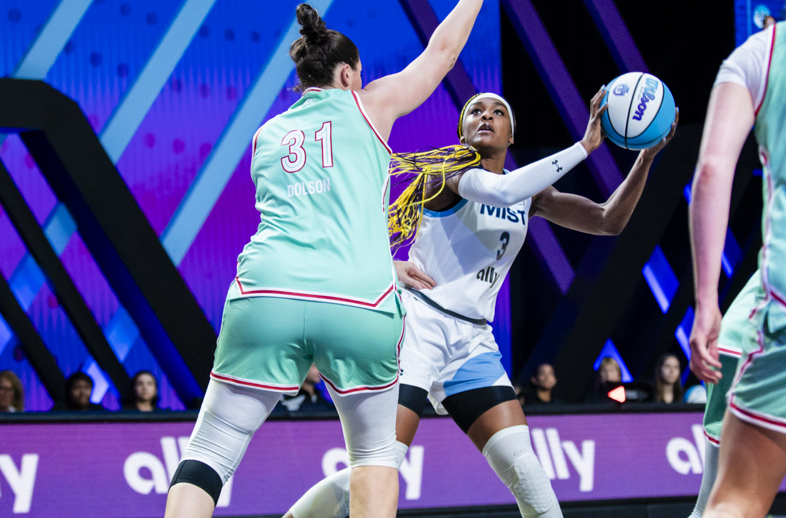 Mist BC forward Aaliyah Edwards holds the ball high on her left side with two hands. She faces the basket and Laces BC center Stefanie Dolson guards her closely, with one hand up to dissuade a shot.