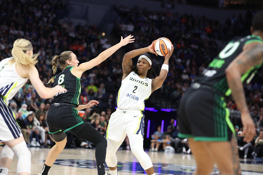 Dallas Wings forward Myisha Hines-Allen holds the ball with two hands. She leans back slightly to get more space from her defender as she looks to make a pass.