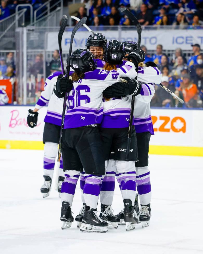 Minnesota players celebrate with a tight group hug by the faceoff circle. They are all wearing white away uniforms.