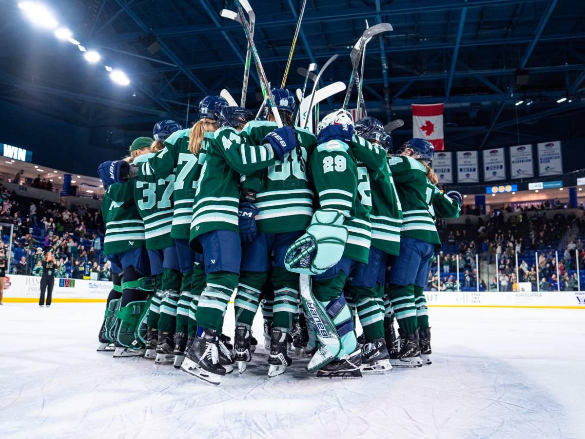 The Boston Fleet celebrate a win with a tight group hug at center ice. They are raising their sticks and wearing green home uniforms.