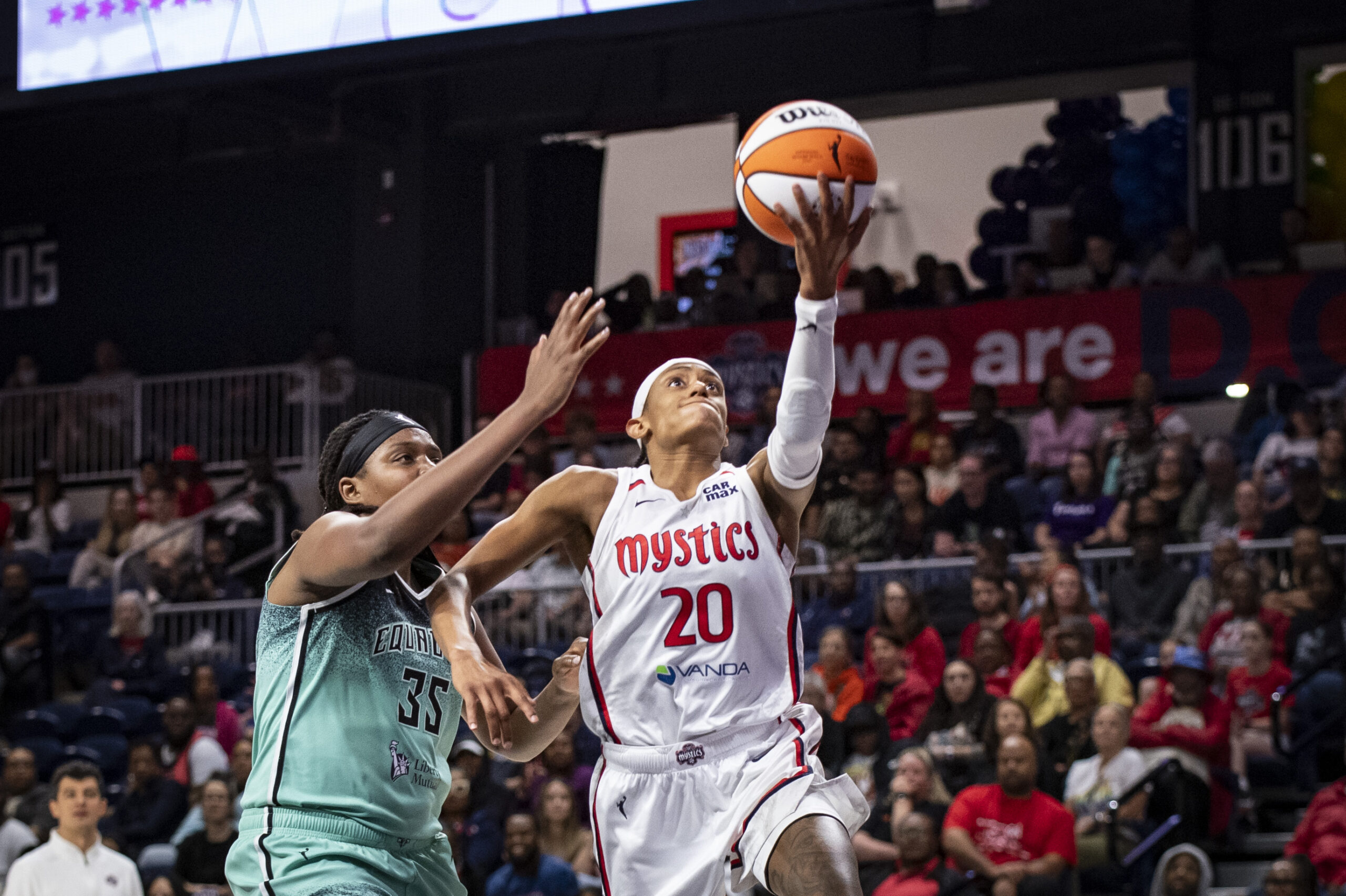 Washington Mystics guard Brittney Sykes extends her left arm in front of her to shoot an underhanded layup. New York Liberty center Jonquel Jones is a step behind her and tries to contest it.