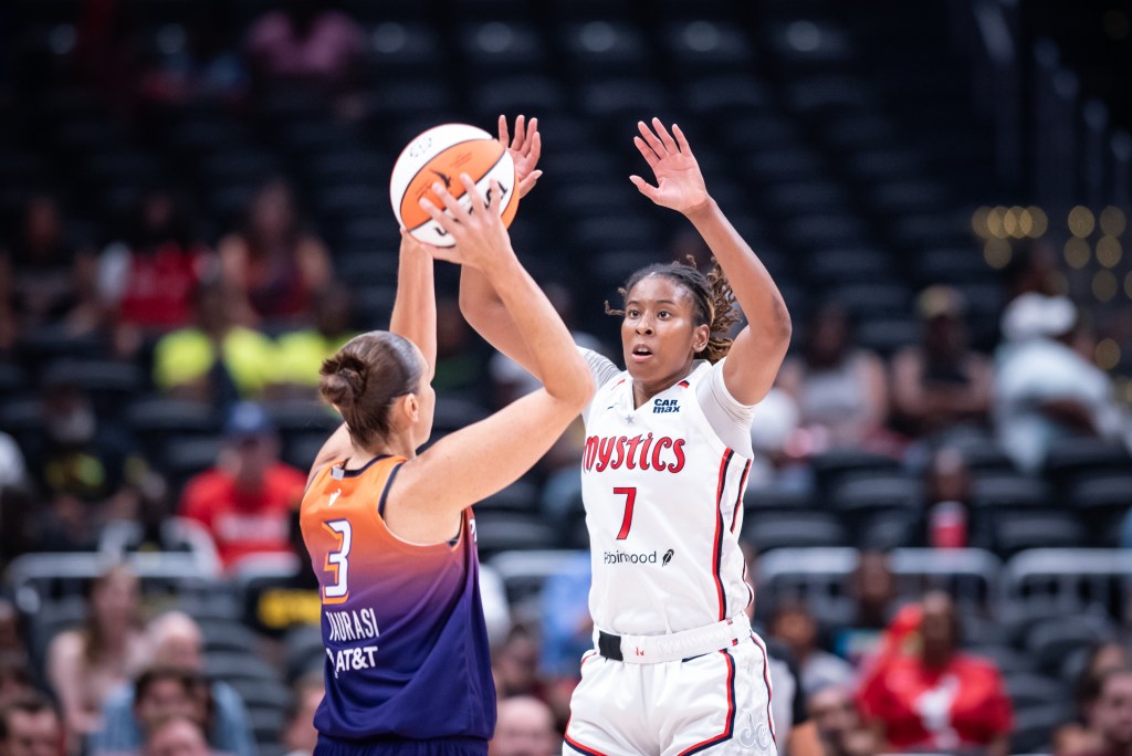 Washington Mystics guard raises both hands while Phoenix Mercury guard Diana Taurasi holds the ball over her head