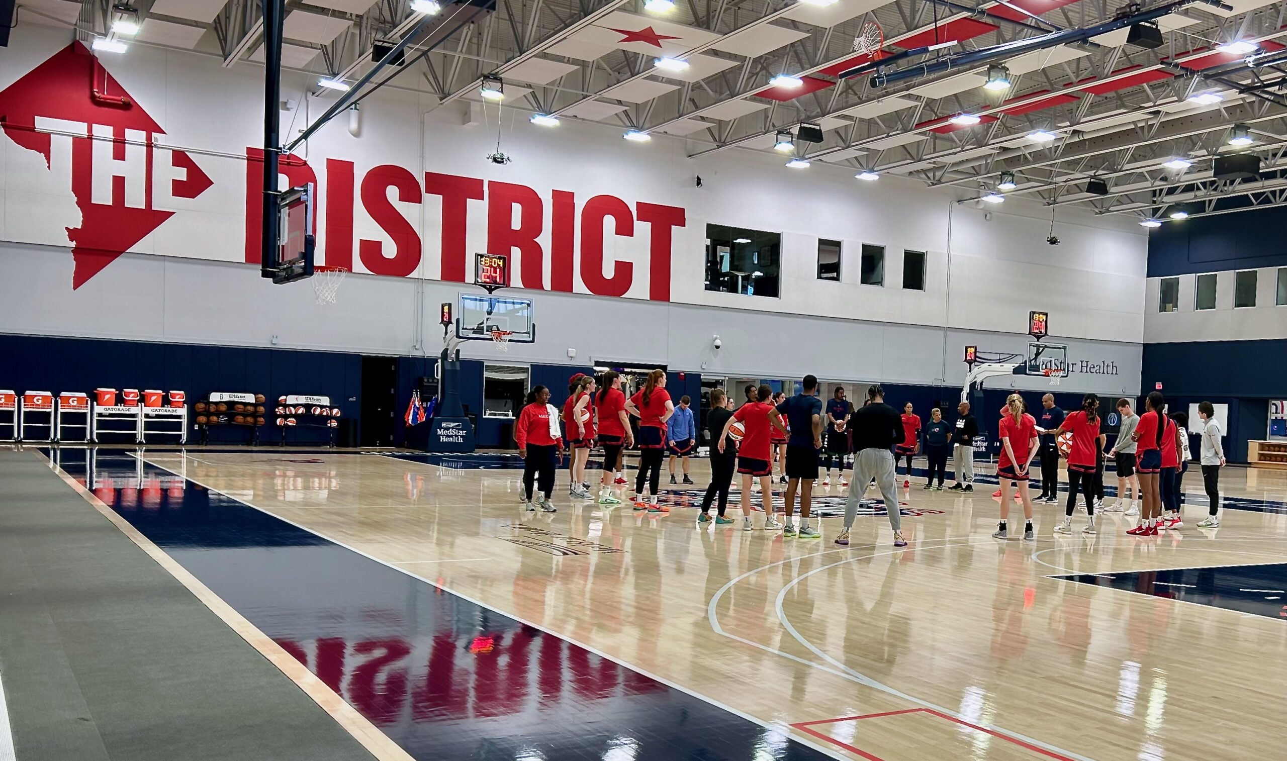 Washington Mystics players and coaches stand in a large circle near the center of the practice court.