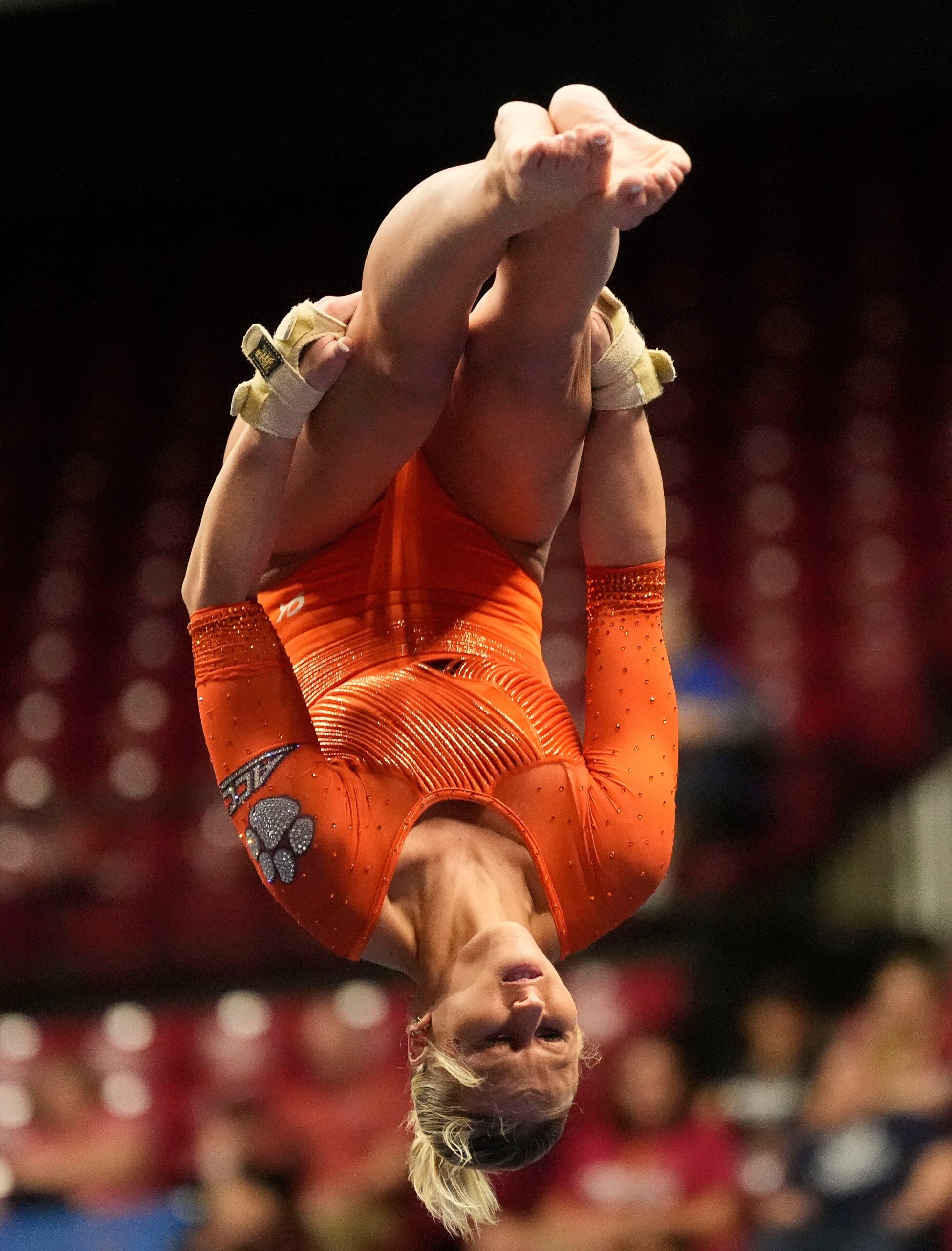 A gymnast in an orange leotard does a flip in the air in a pike position.