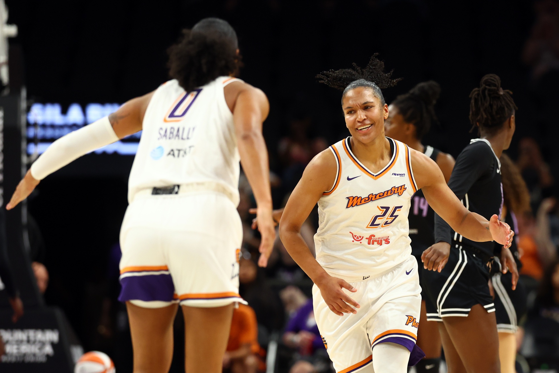Two players, both wearing white uniforms, face each other on the basketball court