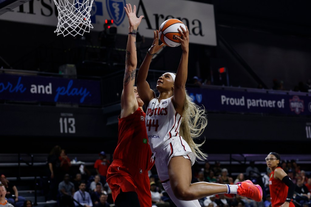 Washington Mystics forward Kiki Iriafen jumps in the air to attempt a left-handed layup. Atlanta Dream center Brittney Griner has her right arm straight up to contest the shot.