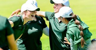 Four golfers huddle together with their arms around one another in celebration. They smile and laugh.