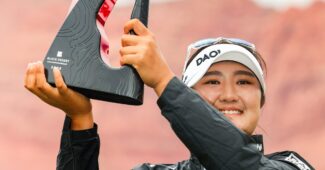 Haeran Ryu holds up a shiny red and textured black Black Desert Championship trophy to her right. She smiles and looks beyond the camera.
