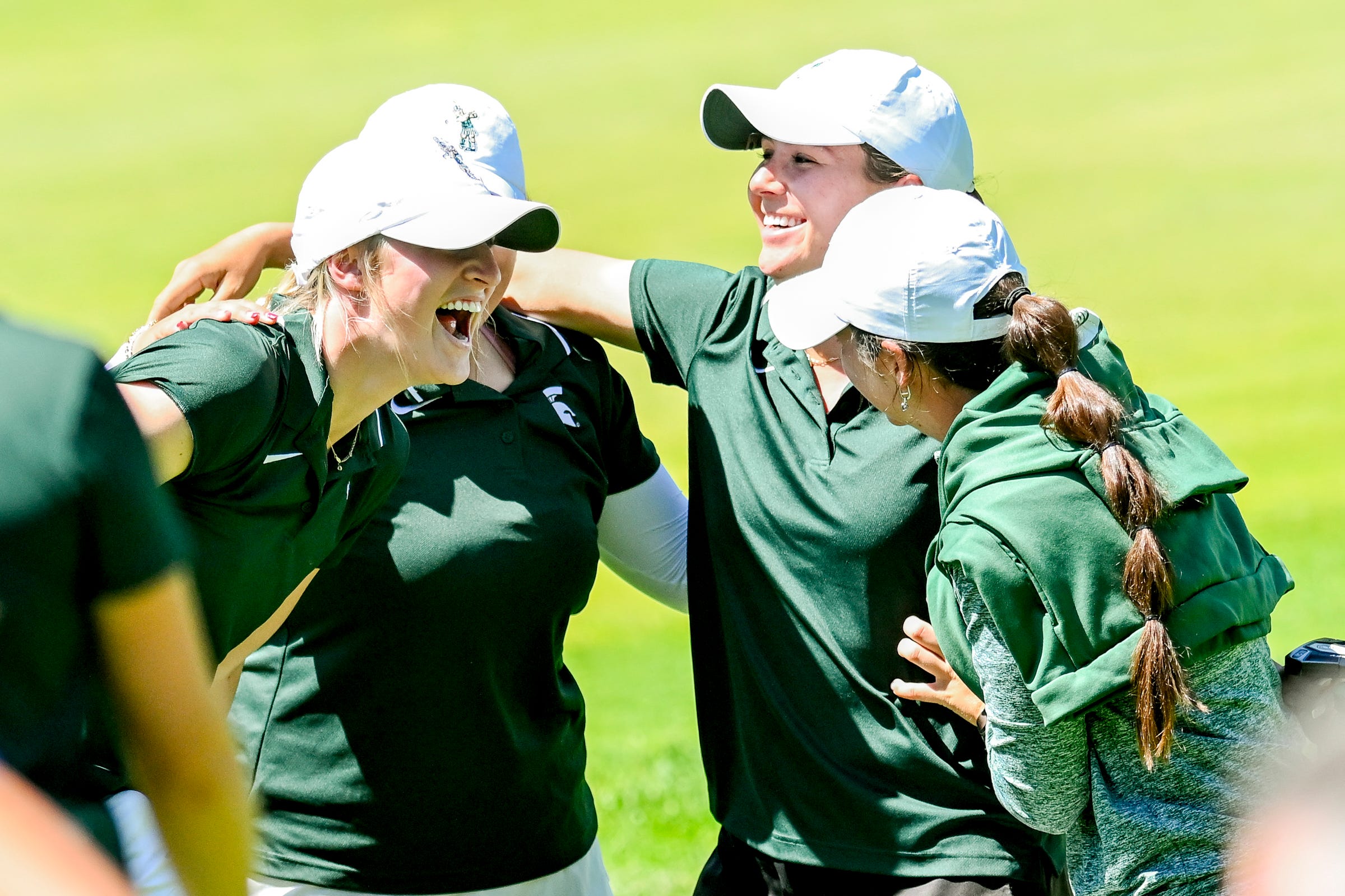 Four golfers huddle together with their arms around one another in celebration. They smile and laugh.