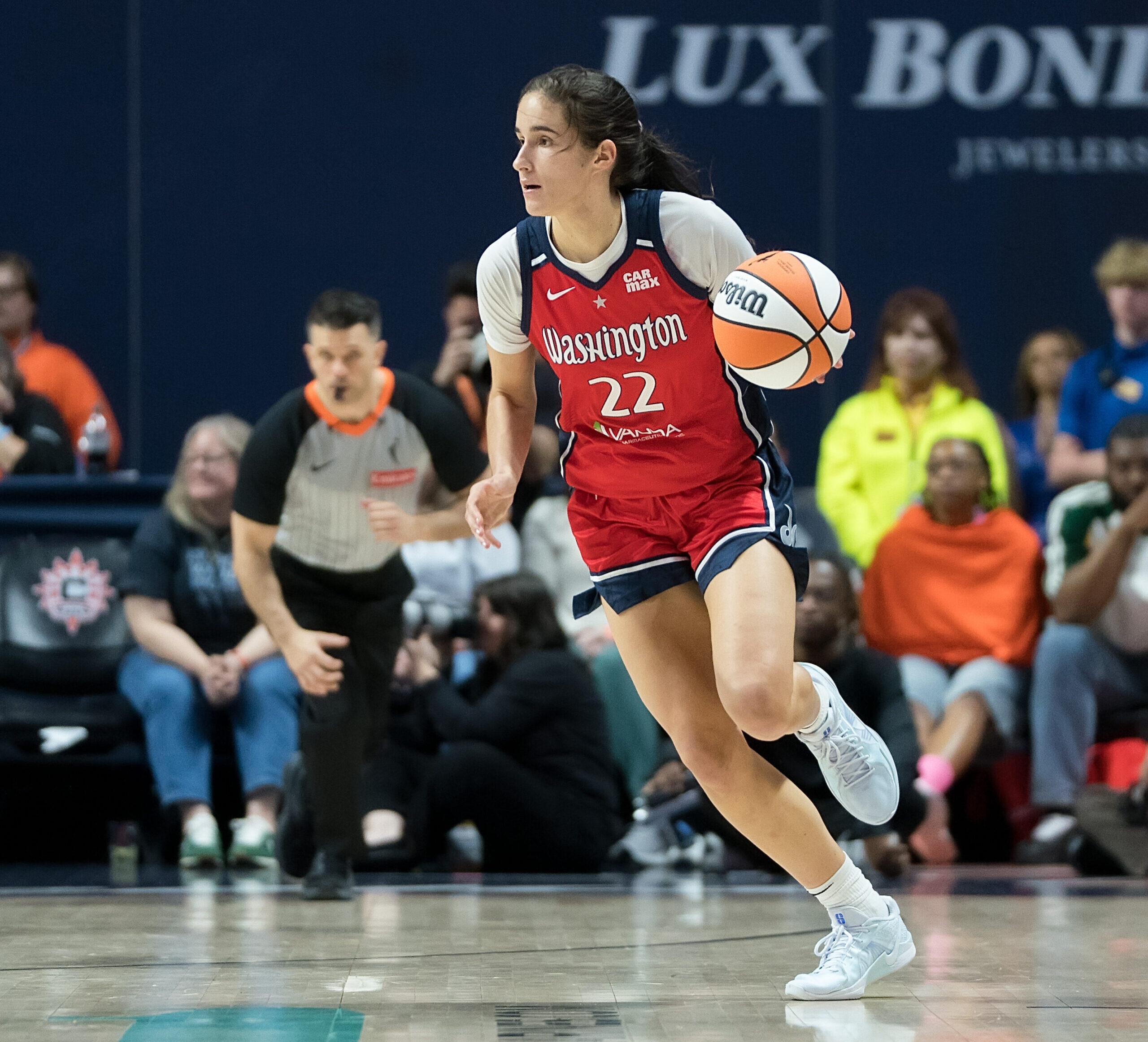 Washington Mystics guard Sonia Citron dribbles the ball with her left hand. She has her eyes up, looking forward and to her right. No defenders are in the frame, but an official is visible running the court behind her.