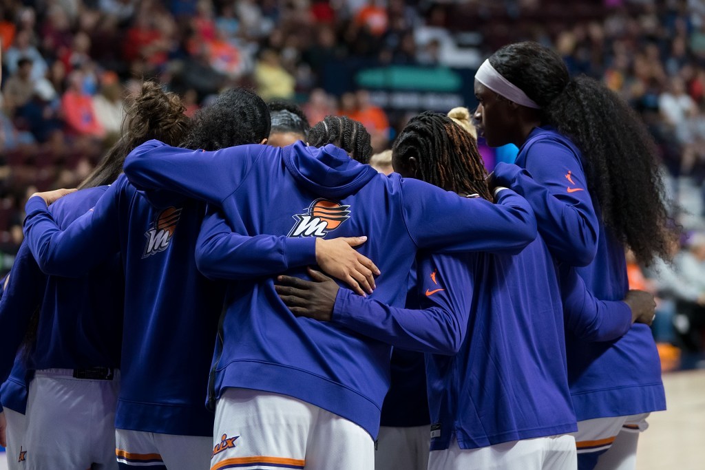 Phoenix Mercury players form a huddle pregame with their arms wrapped around each other.