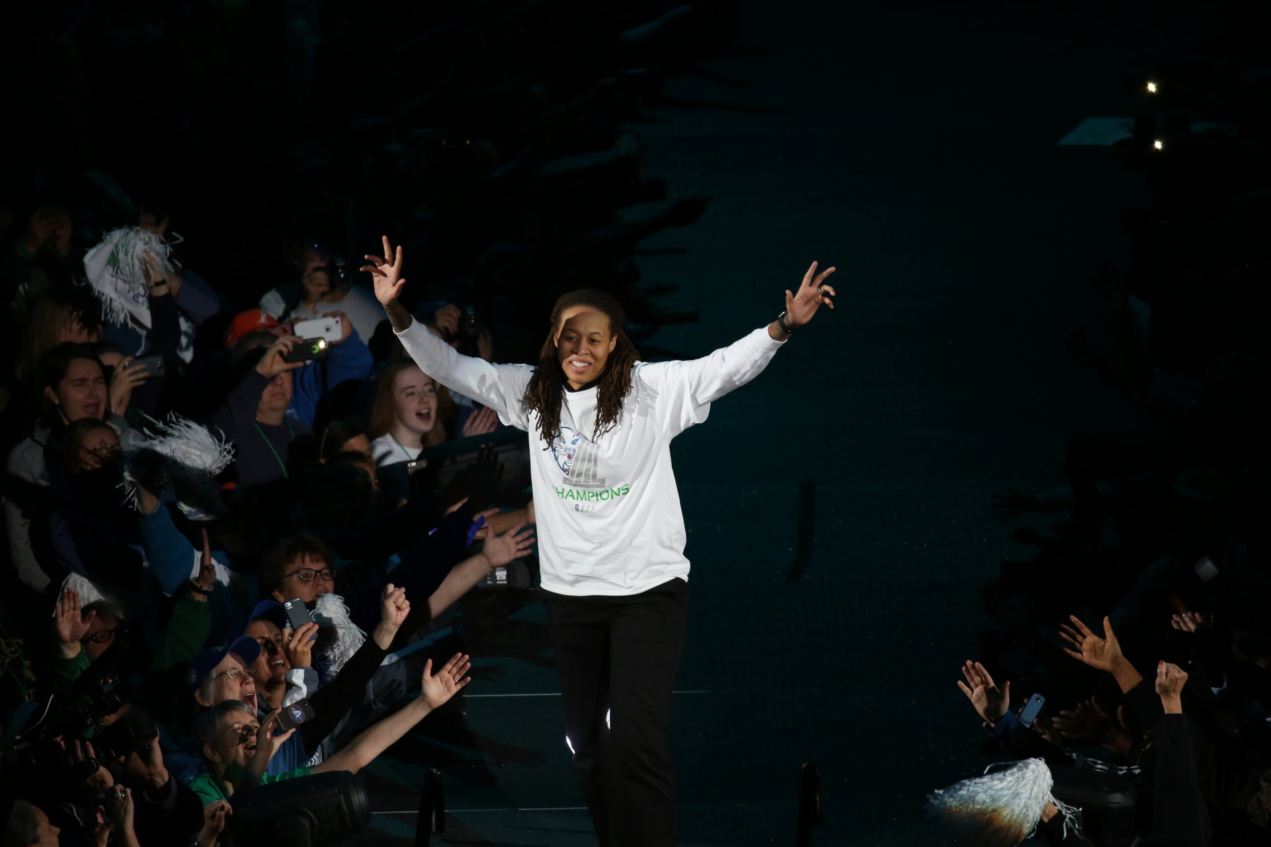 A woman puts her hands up and celebrates at a basketball arena