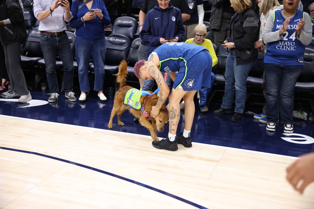 Natisha Hiedeman in her blue Lynx uniform pets a golden retriever on the court