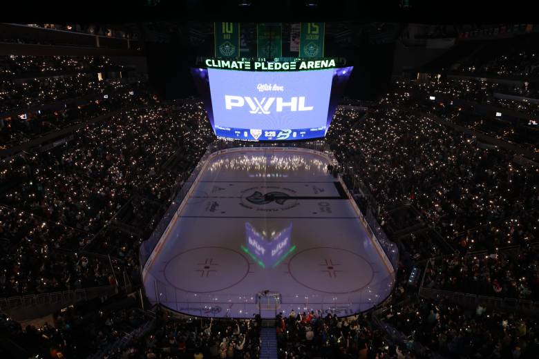 An above-ice view of Climate Pledge Arena during the 2025 PWHL Takeover Tour. The crowd has their phone lights on as the jumbotron displays "with love, PWHL".