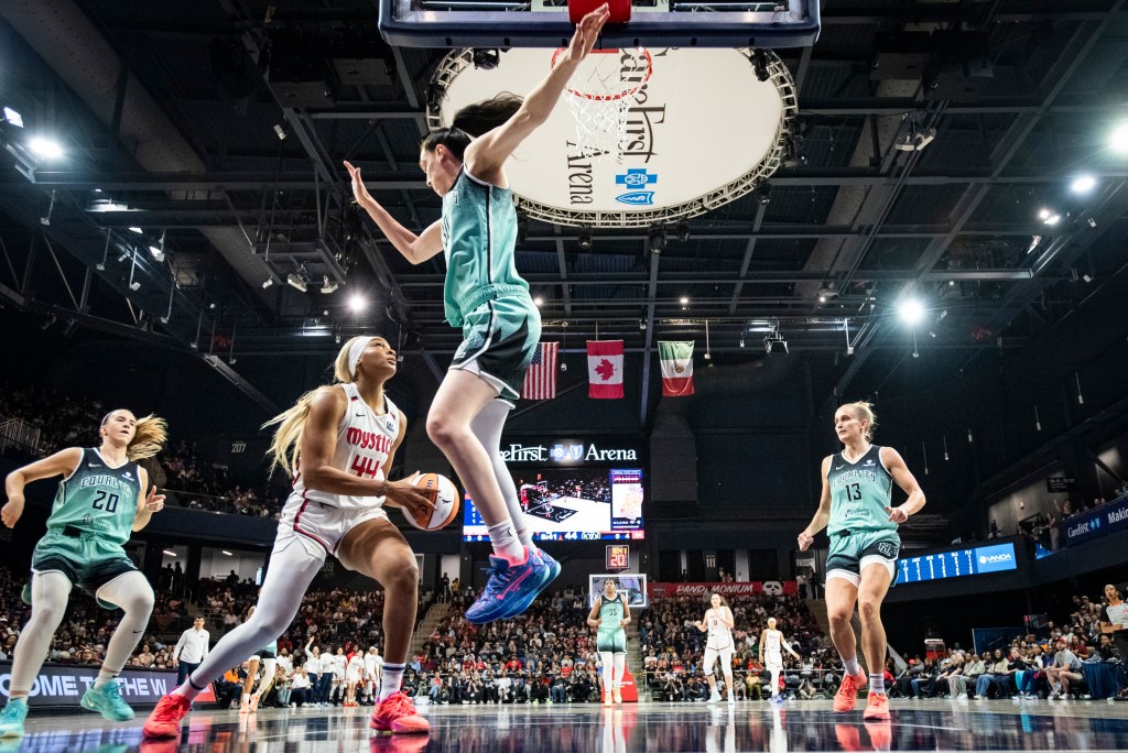Washington Mystics forward Kiki Iriafen holds the ball in the post with two hands as New York Liberty forward Breanna Stewart leaves her feet, anticipating a shot.