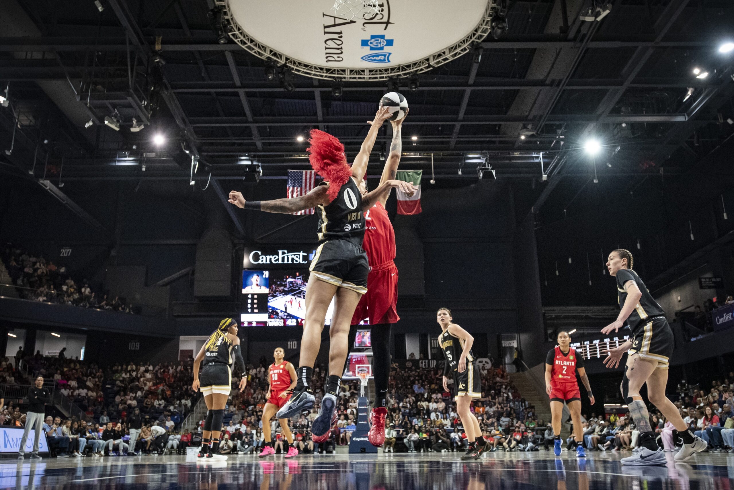 Washington Mystics center/forward Shakira Austin is shown from behind. She is getting her right hand up high enough to block a hook shot from Atlanta Dream center Brittney Griner in the paint.