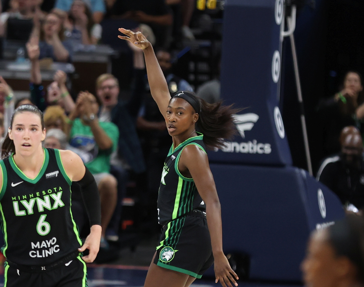 Diamond Miller wears a black jersey puts up three fingers in the background