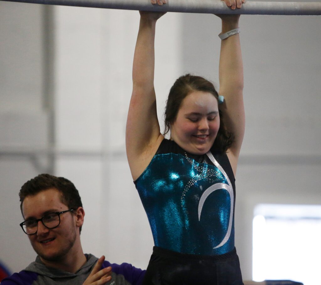 A gymnastic in a black and green leotard competes on the uneven bars at the Special Olympics.