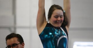 A gymnastic in a black and green leotard competes on the uneven bars at the Special Olympics.