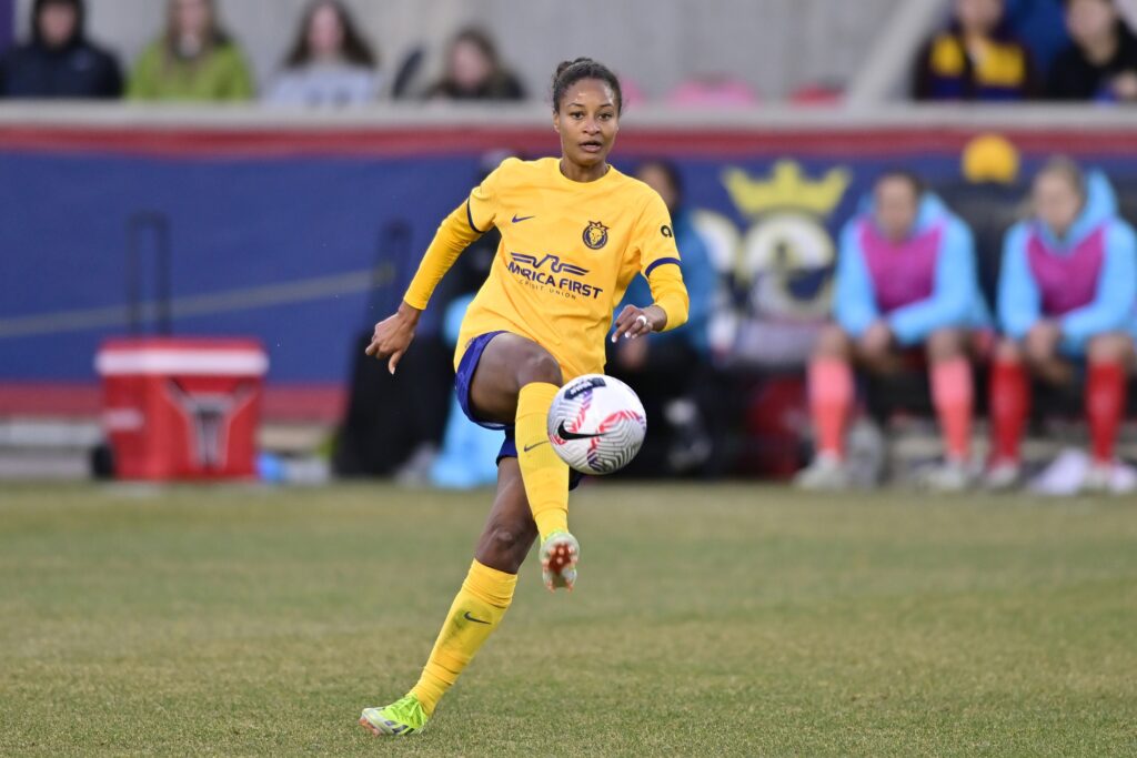 A player wearing a yellow uniform receives the a soccer ball with her shin on the field