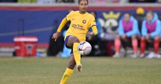 A player wearing a yellow uniform receives the a soccer ball with her shin on the field