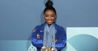 Simone Biles in a blue tracksuit posing with all of her Olympic medals in Paris last summer.