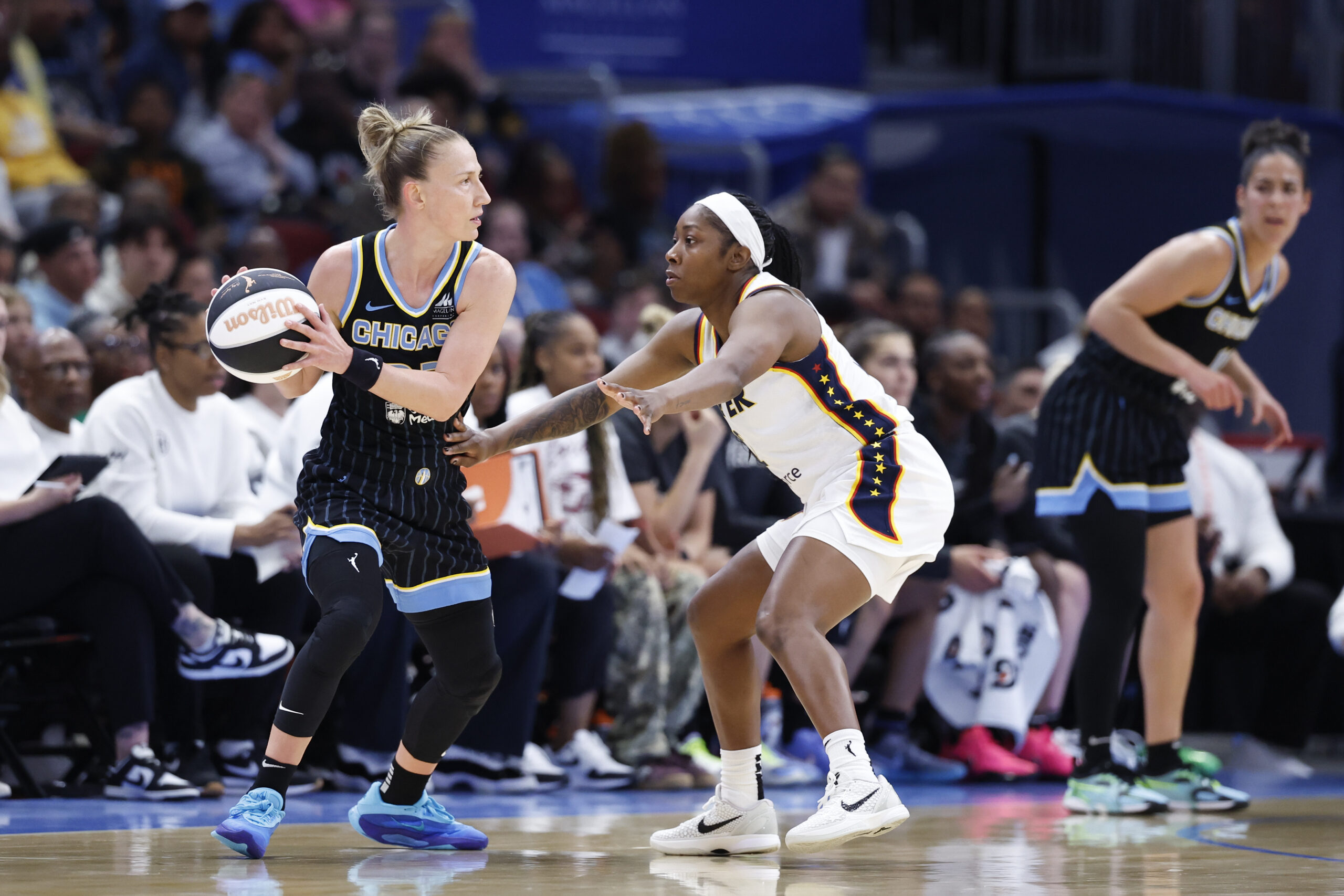 Courtney Vandersloot, wearing a black Chicago Sky uniform, holds the ball with two hands near her right shoulder. She is looking over the shoulder of Indiana Fever guard Aari McDonald, who is in white.