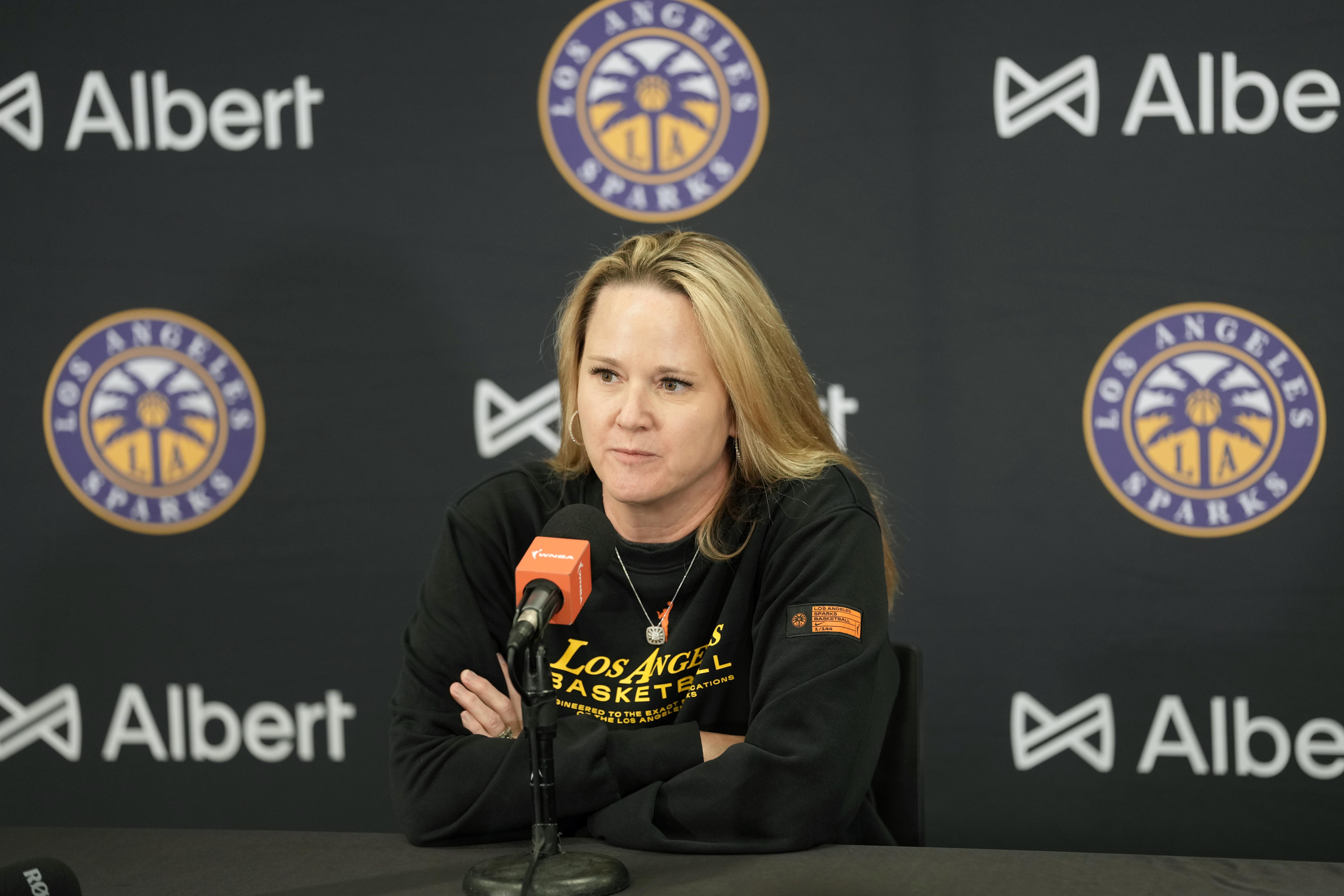 Sparks Head Coach Lynne Roberts addresses reporters ahead of the June 9 game against the Golden State Valkyries, sitting in front of a black background with numerous Sparks logos.