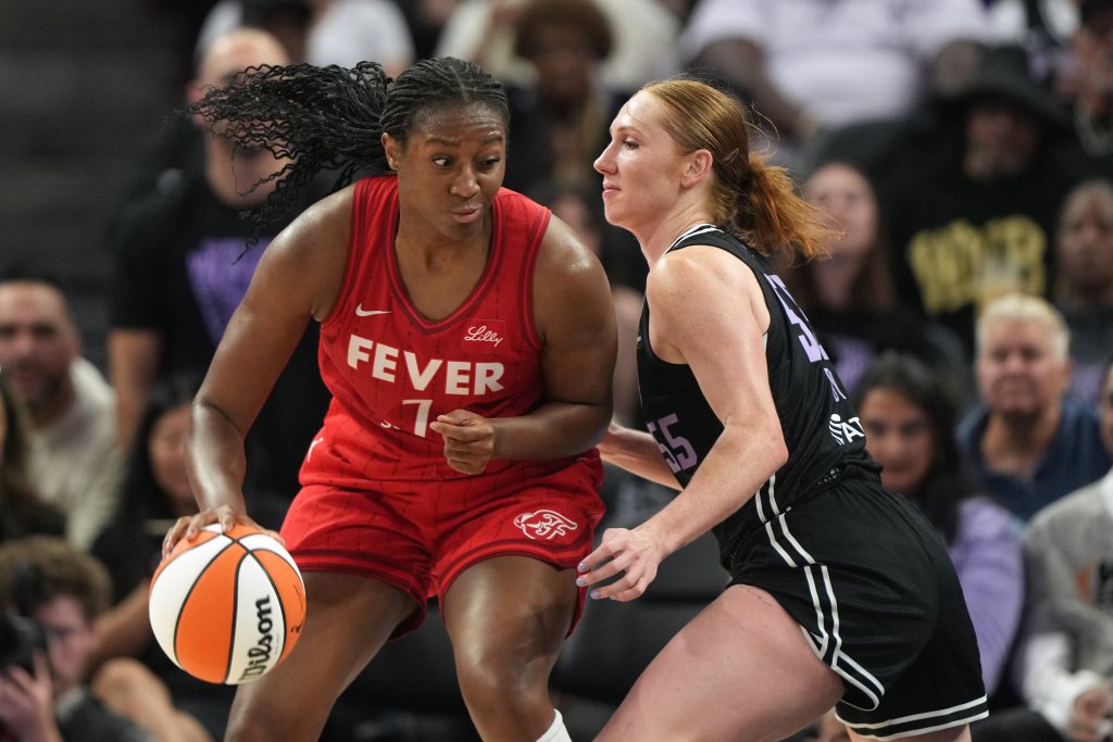 Indiana Fever forward Aliyah Boston dribbles against Golden State Valkyries forward Chloe Bibby. They are shown from the side with some out-of-focus fans in the background behind them.