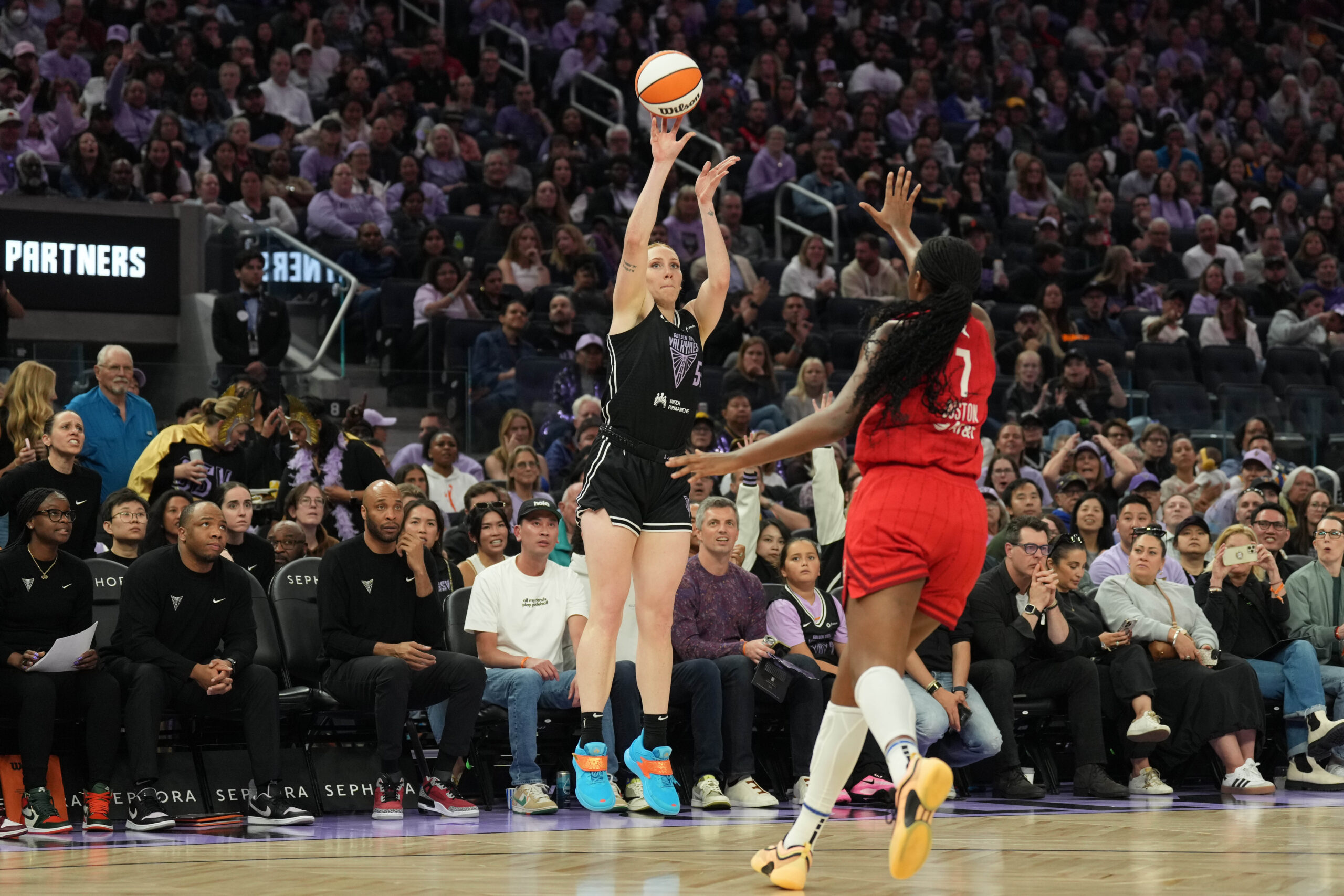 Golden State Valkyries forward Chloe Bibby shoots over Indiana Fever forward Aliyah Boston. She is shown from the front and a packed crowd is in the background behind her.