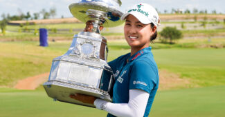 Minjee Lee holds up the KPMG Women's PGA Championship to her left and smiles for a picture. The golf course Fields Ranch East stretches out behind her.