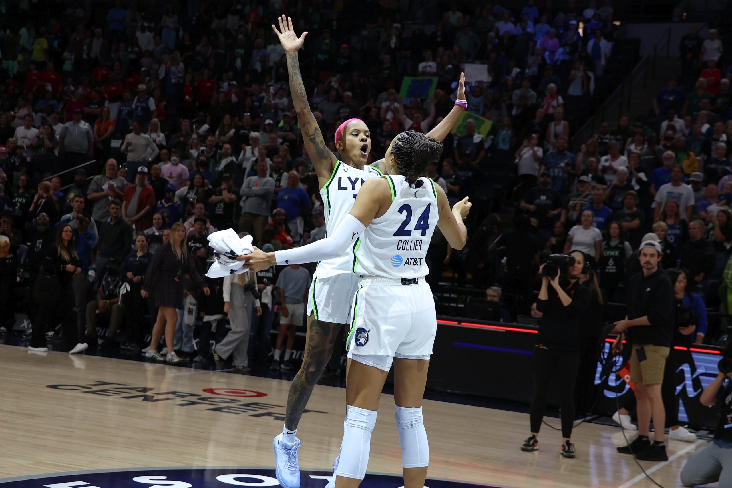 Courtney Williams with pink hair jumps with her arms extended into teammate Napheesa Collier, both in their white Lynx uniforms