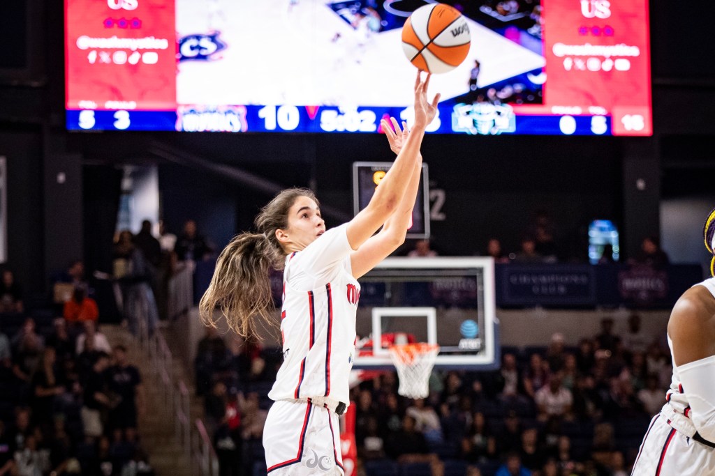 Washington Mystics guard Sonia Citron shoots a wide-open jump shot with her right hand. The bottom of the arena's videoboard and the basket at the other end of the court are visible in the distance behind her.