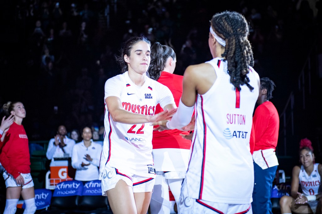 Washington Mystics guard Sonia Citron reaches both hands out in front of her to high-five Sug Sutton, who is standing and waiting for Citron to reach her.